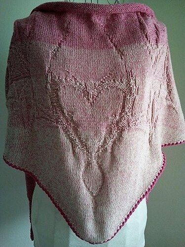 Pink knitted triangle shawl draped on a mannequin showing a central heart lace motif and narrow contrasting edge