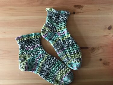 Paar gehäkelter Damensocken aus mehrfarbigem Farbverlaufsgarn auf Holztisch