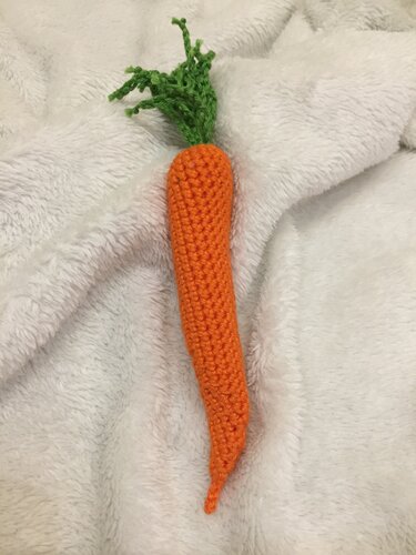 Gehäkelte orange Karotte mit grünen Blattspitzen auf hellem Textil