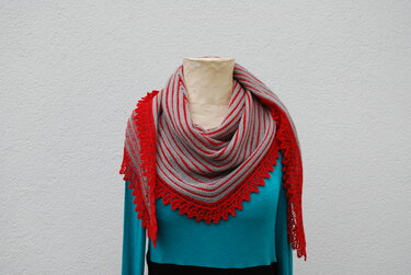 Gestreiftes Dreieckstuch in Rot und Grau mit roter Spitzenborte, drapiert auf einer Schaufensterpuppe über einem türkisfarbenen Oberteil.