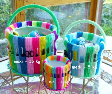 Three striped crochet-covered baskets in three sizes with exterior pockets holding crochet hooks and scissors on a table