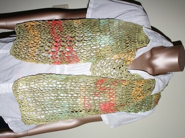 Hellgrüner, offen gestrickter Schal mit roten, orangen und gelben Farbakzenten, drapiert an einer Schaufensterpuppe.