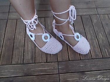 Gehäkelte pastellrosa Ballerinas mit Knöchelband und Deko-Ringen auf Holzdielen