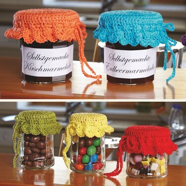 Fünf Gläser mit bunten, handgehäkelten Deckchen, gefüllt mit Marmelade und Süßigkeiten.
