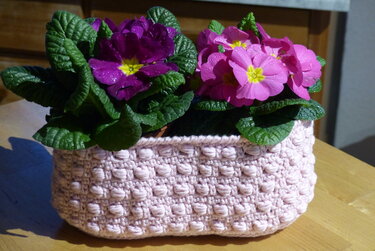 Hellrosafarbener gehäkelter Korb mit Noppenmuster und violett-pinken Primeln