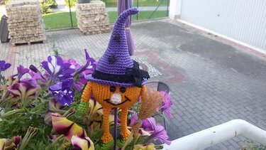 Gehäkelte Kürbis-Hexe mit lila Hut und Besen im Blumenkasten