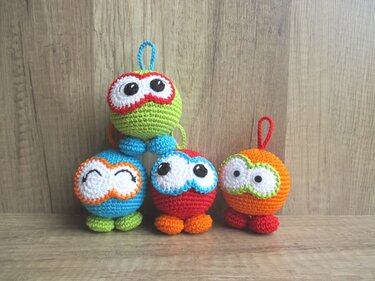Vier handgehäkelte, farbige Figuren mit Schlaufen auf einer Holzfläche.