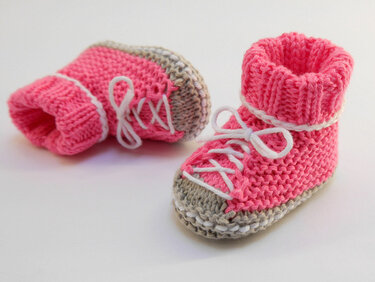 Zwei pinke gestrickte Babyschuhe mit weißen Schnürsenkeln auf hellem Hintergrund