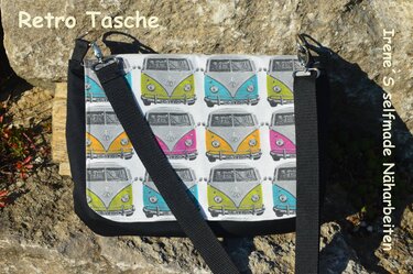 Umhängetasche mit buntem Busmuster, schwarzem Tragegurt und schwarzer Einfassung auf Felsen