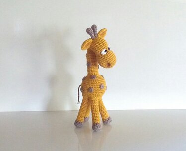 Gehäkelte Amigurumi-Giraffe in Gelb mit lila Tupfen auf hellem Hintergrund