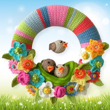 Gehäkelter bunter Kranz mit Blumen, grünen Blättern und drei kleinen Vögeln, zwei im Nest