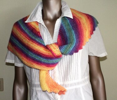 Gestrickter Drachenschwanzschal in Regenbogenfarben, an einer Schaufensterpuppe drapiert.