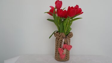 Rote Tulpen in Vase mit braun gehäkelter Hülle und rosafarbenen Herzen am Band