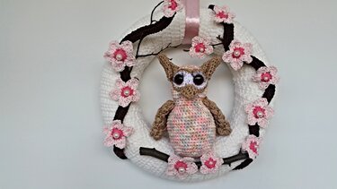 Weißer gehäkelter Türkranz mit mittiger gehäkelter Eule, braunen Zweigen und rosa Blüten mit Perlen, aufgehängt an rosafarbenem Band