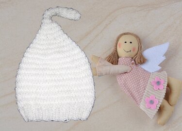 Weiße gestrickte Zipfel‑Babymütze neben einer Stoffpuppe