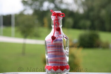 Glasflasche gefüllt mit geschichtetem buntem Sand und roten Herzverzierungen