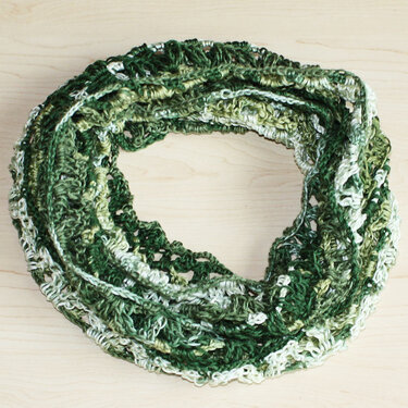 Gehäkelter Loop-Schal in grünen Farbabstufungen auf hellem Holzuntergrund