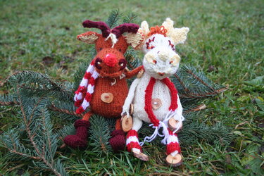 Zwei gestrickte Amigurumi-Rentiere mit rot-weiß gestreiften Schals auf Tannenzweigen