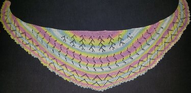 Halbrundes gestricktes Tuch mit Lochmuster in Pastellfarben auf dunklem Hintergrund.