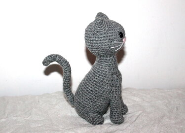 Gehäkelte graue Amigurumi-Katze sitzend seitlich mit gebogenem Schwanz