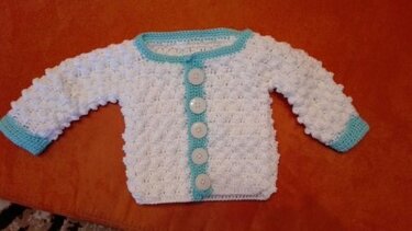 Weiße gehäkelte Babyjacke mit türkisfarbener Einfassung und fünf Knöpfen, flach ausgelegt