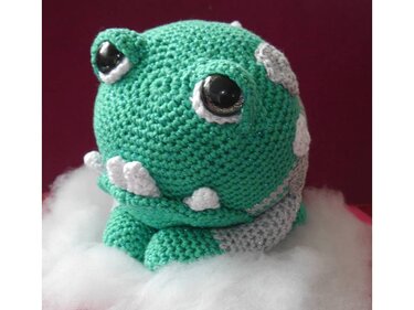 Grünes und graues gehäkeltes Amigurumi mit weißen Tupfen und schwarzen Sicherheitsaugen