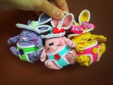 Drei gehäkelte Amigurumi-Osterhasen in Pastellfarben mit Hüten und Knöpfen