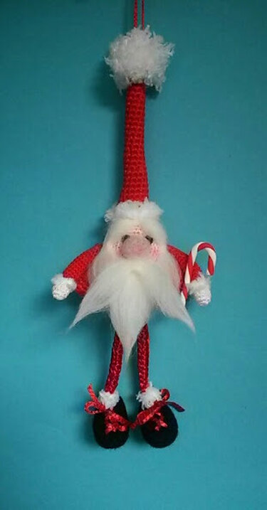 Gehäkelter Weihnachtsmann-Amigurumi mit langer roter Zipfelmütze, weißem Bart und Zuckerstange, hängend vor blauem Hintergrund