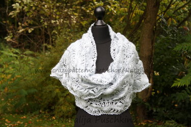 Lichtblauer gehäkelter Loop mit filigranem Spitzenmuster auf schwarzer Schneiderpuppe vor Pflanzen