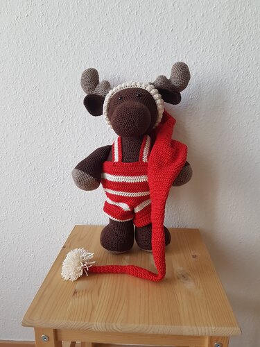 Gehäkelter Amigurumi-Elch mit rot-weiß gestreiftem Latzhöschen und langer roter Zipfelmütze mit hellem Bommel