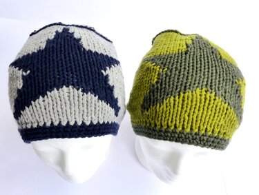 Zwei gestrickte Beanies mit kontrastierendem Sternmuster auf weißen Schaufensterköpfen; links dunkelblau/hellgrau, rechts olivgrün/gelbgrün
