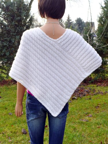 Rückenansicht einer Person mit weißem gestricktem Poncho mit diagonalem Zopfmuster, kombiniert zu Jeans