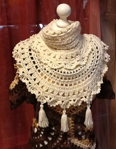Cremefarbener, gehäkelter Kragenschal mit hohem Kragen und Quasten auf einer Schneiderpuppe.