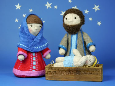Knitted Mary and Joseph standing beside a knitted baby in a wooden manger on a blue background with star decorations