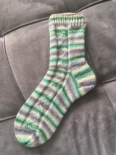 Gestrickte Damen-Socke in Grün, Grau und Beige mit Streifen und Zopfmuster auf dunklem Untergrund