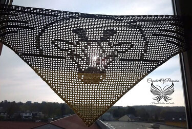 Gehäkeltes dreieckiges Filet-Tuch mit Stierkopf-Motiv vor hellem Fenster