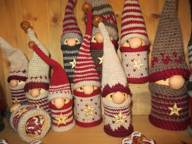 Gehäkelte Wichtel in Rot und Grau mit spitzen Mützen und nummerierten Holzsternen auf einem Holzregal