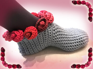 Gehäkelter grauer Slipper mit gehäkelter Rosenborte am oberen Rand, getragen an einem dunklen Bein.