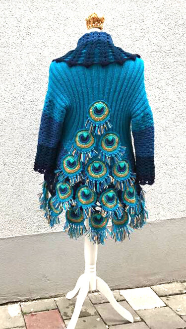 Back view of a teal and blue crocheted women's jacket on a mannequin, featuring layered peacock-feather circular appliques and fringe.