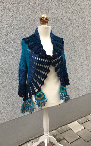 Mannequin wearing teal-to-navy open-front crochet jacket with lacy panels and fringed circular medallions