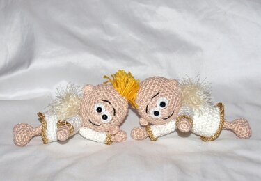 Zwei gehäkelte Amigurumi‑Engel mit Flügeln und goldenen Details auf hellem Stoff