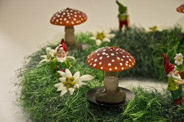 Runder grüner Deko-Kranz mit roten Fliegenpilzen, Zwergenfiguren und weißen Edelweißblüten.