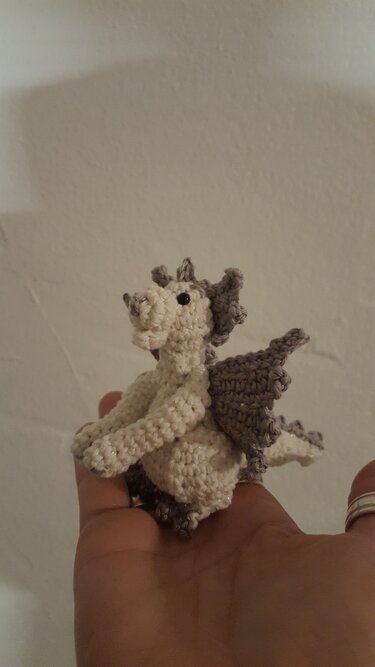 Gehäkelter Mini-Amigurumi-Drache in Creme und Grau auf einer Hand