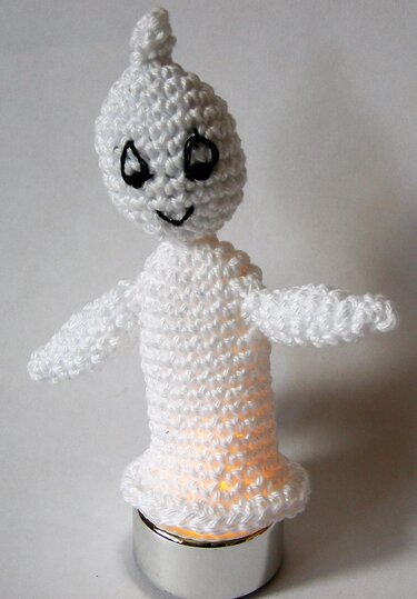 Gehäkelter weißer Amigurumi-Geist mit aufgesticktem Gesicht, beleuchtet von einem Teelicht.