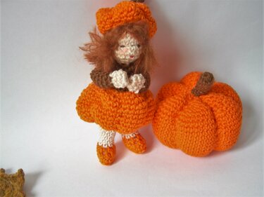 Gehäkelte Amigurumi‑Puppe im orangefarbenen Kürbiskleid neben einem gehäkelten Kürbis