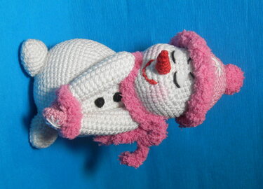 Gehäkelter weißer Schneemann mit rosa Mütze und Schal vor blauem Hintergrund