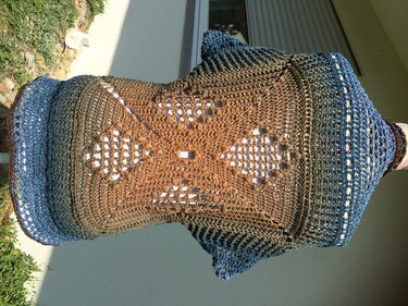 Gehäkelter Seelenwärmer in Braun und Blau mit zentralem Lochmuster, auf Schaufensterpuppe im Freien.