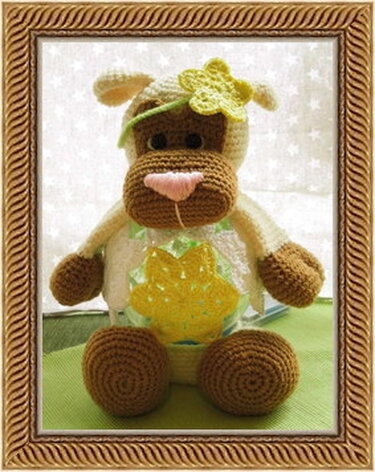 Gehäkelte sitzende Kuh in Weiß und Braun mit gelber Sonnenapplikation und grüner Blüte