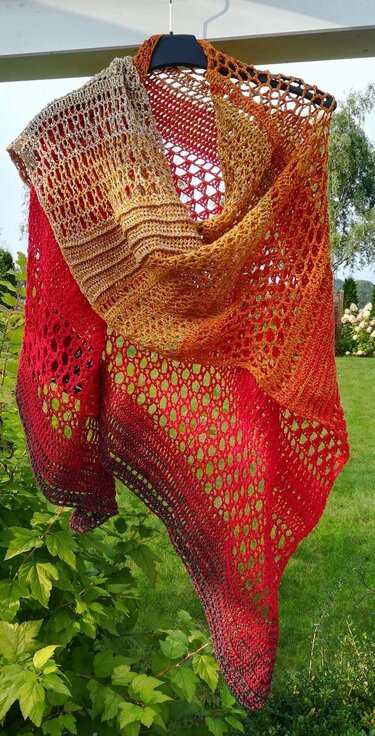 Crocheted dragon tail scarf in beige, orange and red ombre with lace and textured stitches, hanging on a hanger outdoors.