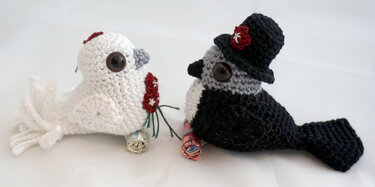 Zwei gehäkelte Amigurumi-Vögel, weiße Braut mit Blumenstrauß und dunkler Bräutigamsvogel mit Zylinder